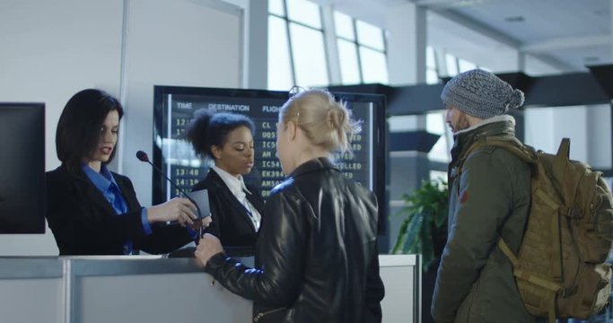 Airport security personnel processing passengers at a check-in counter in a departures or arrivals hall checking their identity against passports and thumb prints. 4K shot on Red cinema camera.
