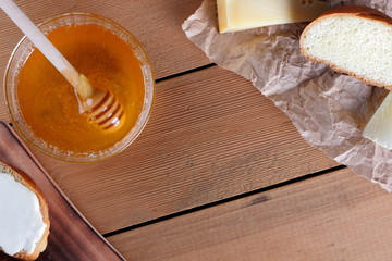 Hard cheese on a wooden board, food on parchment paper, sandwiches with soft cheese, honey in glass dishes, copy space, cheese pattern, wood background, wooden cutlery, simple food