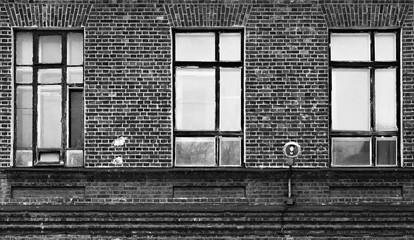 Fragment fasady starego budynku z cegły. Wysokie okna i materiały teksturowane. - 196407248