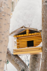 Wooden bird feeder from small logs of light brown color between the trees under the snow
