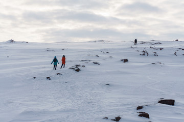 Two young girls in bright jackets travel on snowy peaks of the tundra in winter in a frost drowning in the snow