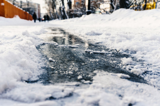Slippery shiny ice on the sidewalk in winter under the snow beckons to ride on it to enjoy