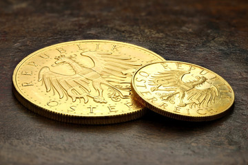 Austrian 25 and 100 Schilling gold coins on rustic wooden background