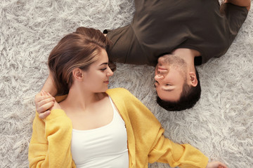 Cute young lovely couple lying on carpet at home