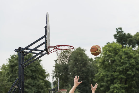 Street basketball game. Basketball shield, Basket and ball on background of sky, street in summer. Hands of Basketball player throwing ball into basket
