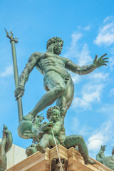 Fototapeta na wymiar Detail close up of 1500s Bologna Neptune statue-fountain of Bologna city in Italy. Restored in 2018 and located in Nettuno square of Bologna city center. Vertical lower ground view with blue sky.