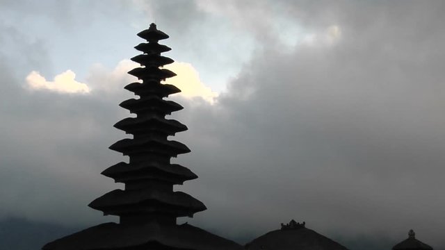 A Balinese temple stands silhouetted against a cloudy sky.