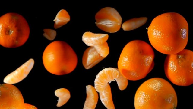 Slices and whole mandarins bouncing against to the camera on a black background in slow motion