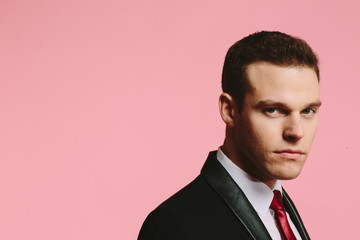 Handsome young man in black suit and tie on pink background