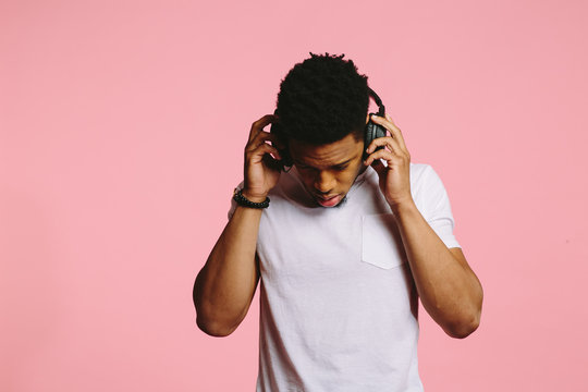Portrait of a cool man listening to music on headphones and looking down, isolated on pink background