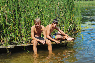 Two boys, a teenager rest on the river bank, on a hot day