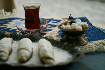 Mutaki roll cake with walnuts and sugar powder, oriental sweets mutaki pastry and traditional glass of black tea on rustic wooden blue table background, close-up