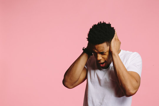 Portrait of a young man in white shirt holding his head in distress, on pink background