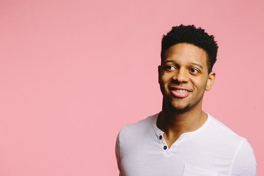 Portrait of a smiling African American guy looking sideways on pink background