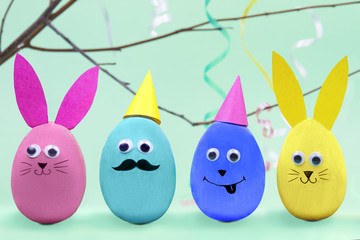 Happy Easter concept. Colorful easter eggs with comic fun faces on blue background with tree branch and colorful curve tapes