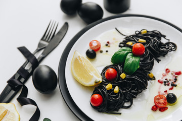 Black spaghetti with basilica and tomatoes on table. Black Easter eggs.