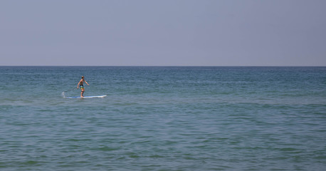 A teenage boy paddle boarding in the ocean.