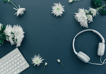 Headphones and computer keyboard on blue table with flowers. Flat lay. Call center concept