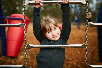 young girl playing hanging on monkey bars being silly