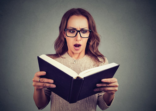 Surprised woman reading book in eyeglasses