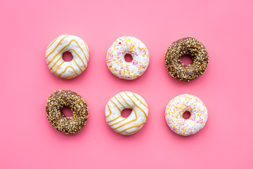 Donuts decorated icing and sprinkles on pink background top view pattern