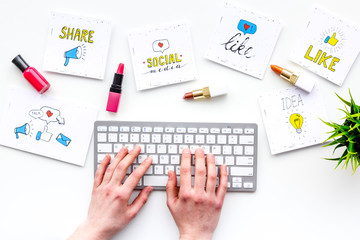 Female blogger concept. Work desk with keyboard, cosmetics and social media icons on white desk top view. Hand is typing