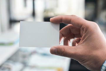 Closeup on hand of a person holding showing white business card over blurry office background
