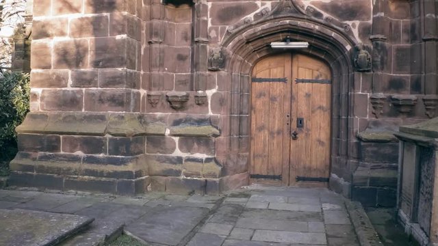 view on entrance of old sandstone church. later camera shows tower with clock and english flag