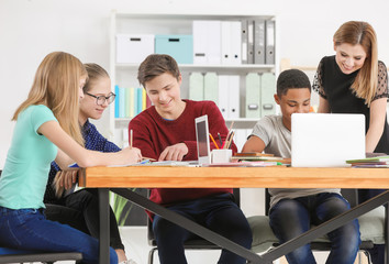 Group of teenagers doing homework with teacher in classroom