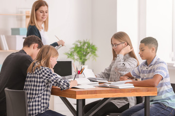 Group of teenagers doing homework with teacher in classroom