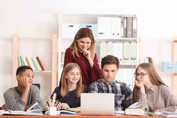Group of teenagers doing homework with teacher in classroom
