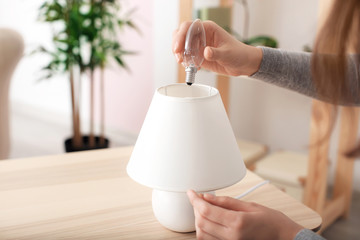 Woman changing light bulb in lamp at home