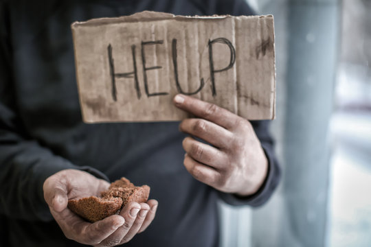 Poor man holding piece of cardboard with word HELP and bread, closeup