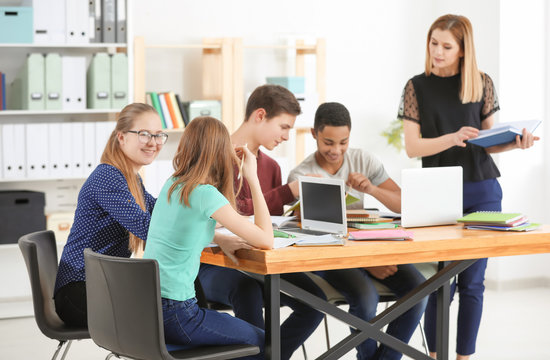 Group of teenagers doing homework with teacher in classroom
