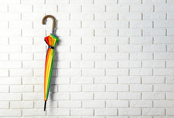 Stylish rainbow umbrella hanging on brick wall