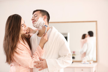 Obraz na płótnie Canvas Young woman helping her boyfriend shaving in bathroom