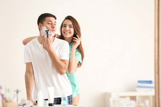 Young man shaving and his girlfriend in bathroom