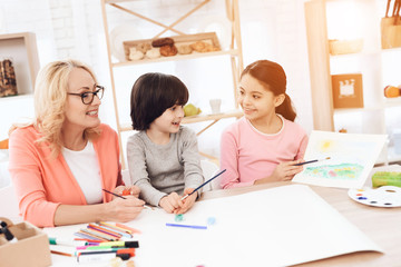 Fototapeta premium Beautiful egrandmother teaches grandchildren to draw. Children draw with paints.