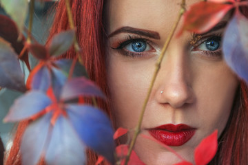Close up of a beautiful red head woman among the colorful autumn leaves