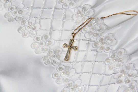 Sparkling gold cross with heart & chain on white first communion, baptism, christening, wedding dress gown with pearls, sequins, cross stitch embroidery, & little flowers.