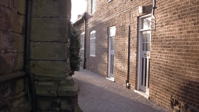 View on brick wall with white windows and doors next to old sandstone church wall. Quiet alley in small village.