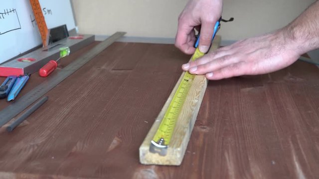Measure with a tape measure. Thin bar. Men's hand. Country style. Wooden table. The tools in the background. Workshop. Video 4k.