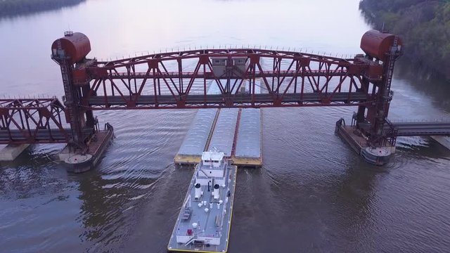 A beautiful aerial of a barge traveling on the Mississippi River under a large steel drawbridge.