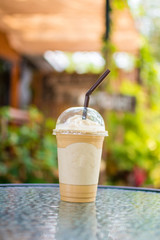 ice coffee frappe on glass table with nature background. subject is blurred.