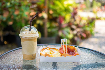 ice coffee with bread and jam on table with nature background. subject is blurred.