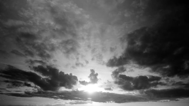 Timelapse of a cloudscape in black and white with dark clouds passing in front of the sun in late evening, before sunset. Cumulus and stratocumulus in a sky becoming clearer, showing a low sun.