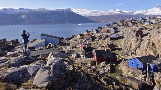 Panning motion of a hiker overlooking colorful homes and Karajak Fjord from Qilakitsoq in Uummannaq, Greenland. 