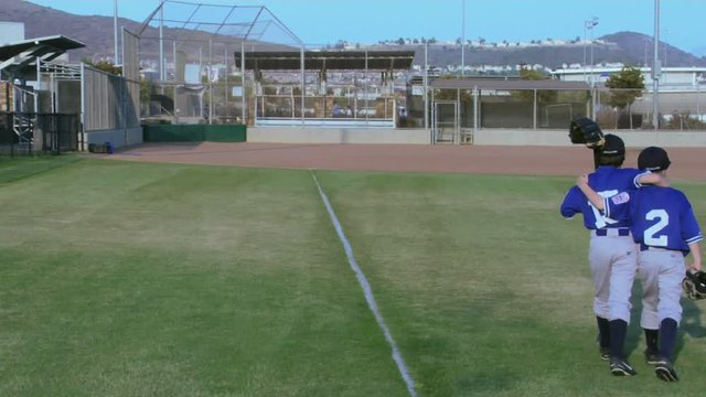 Little league baseball players place their arms around one another as they walk.