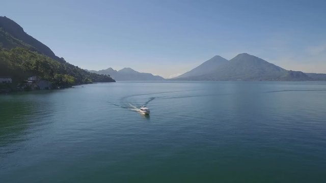 Aerial over a boat on Lake Amatitlan in Guatemala reveals the Pacaya Volcano in the distance.