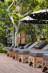 Deck chairs and umbrellas in tropical garden near swimming pool on the beach in Bali, Indonesia